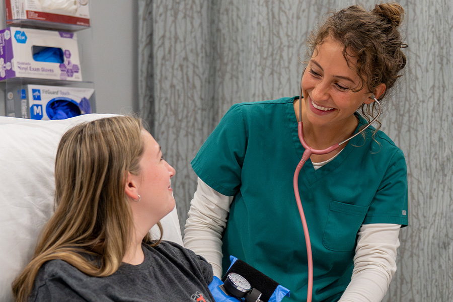 Nursing student in scrubs smiles while checking a patient's blood pressure